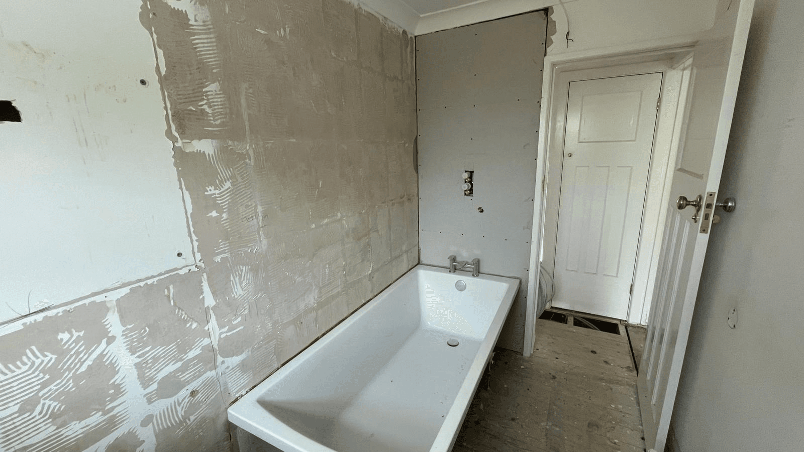 Bathroom in progress — bath positioned, walls plastered and ready for tiling