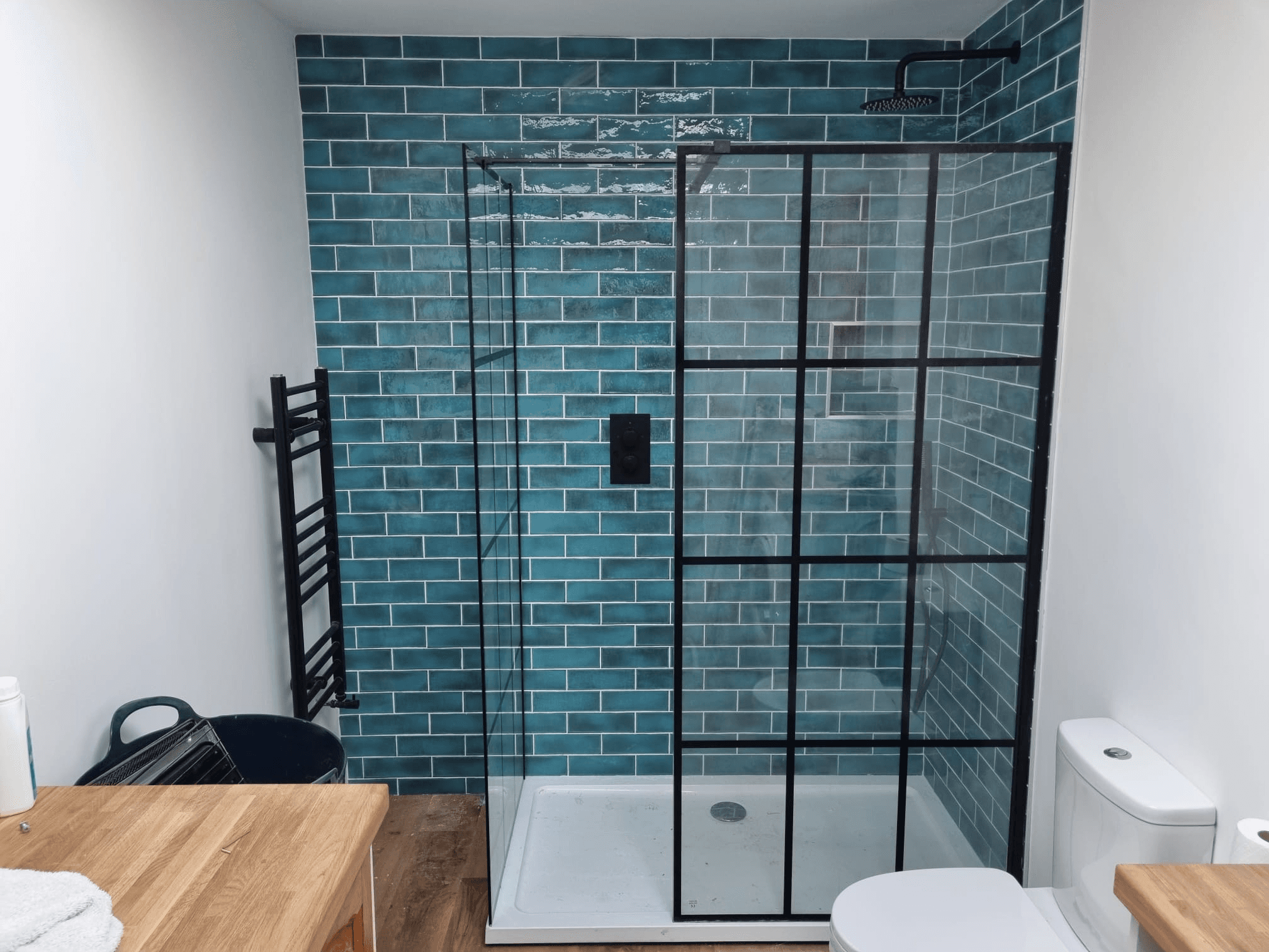Completed walk-in shower — teal metro tiles with black Crittall-style shower screen