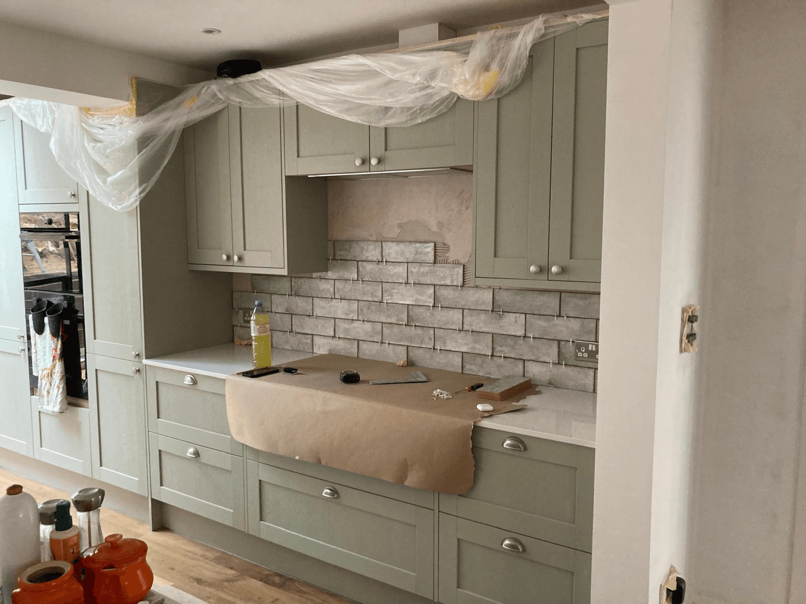 Sage green shaker kitchen being installed — brick tile splashback and integrated appliances